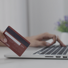 Person using a laptop and holding a bank card